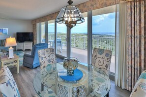 A room with a balcony, a television, a dining table with chairs, and a decorative bowl.