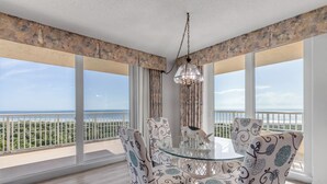 A dining area with a glass table and patterned chairs, overlooking a balcony with a view of the sea. - Ravishing Panoramic Vista | Inlet #608 (New Smyrna Beach)