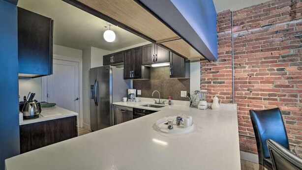 Une cuisine moderne dotée d’un grand îlot central, de meubles de couleur sombre et d’un mur en briques.