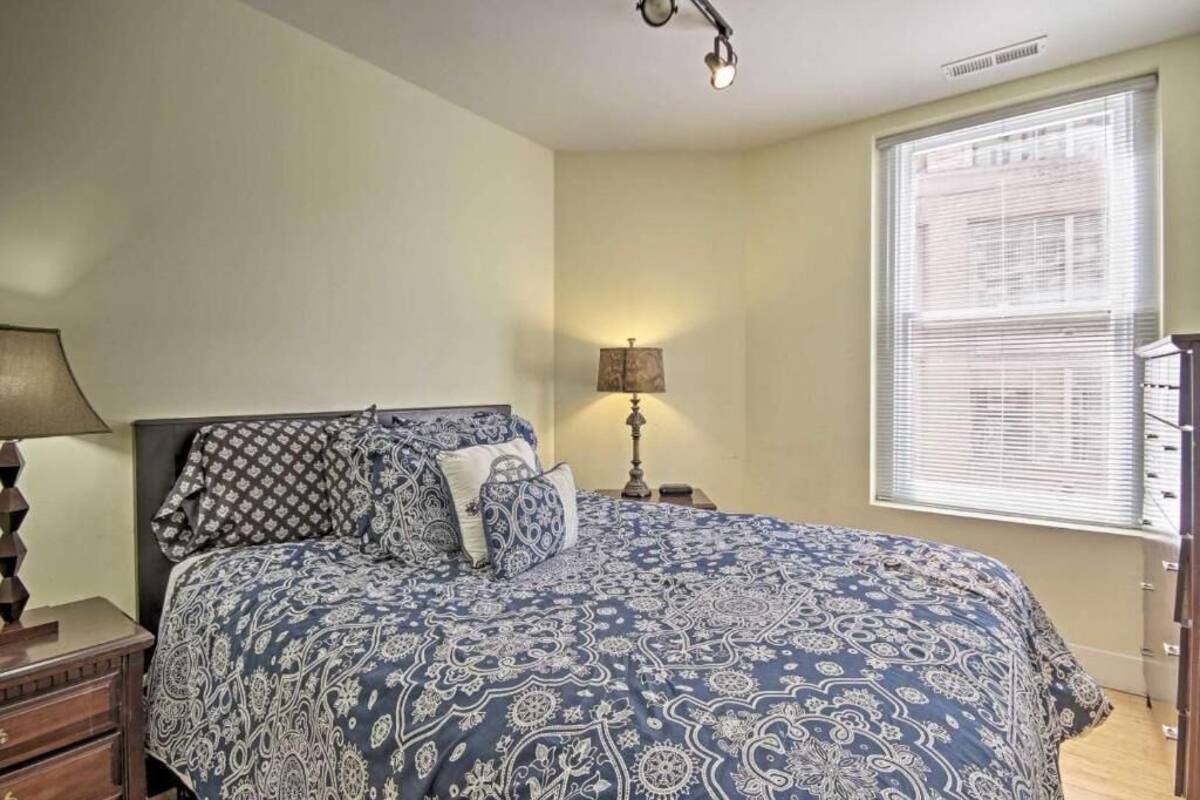 A bedroom with a large bed, a nightstand, a lamp, and a window with blinds.