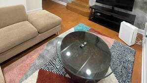 Una sala de estar con un sofá, una mesa de centro de vidrio, un televisor y una escalera que sube a otro nivel.