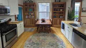 Una cocina con armarios blancos, una mesa de comedor de madera, microondas, estufa y lavavajillas.