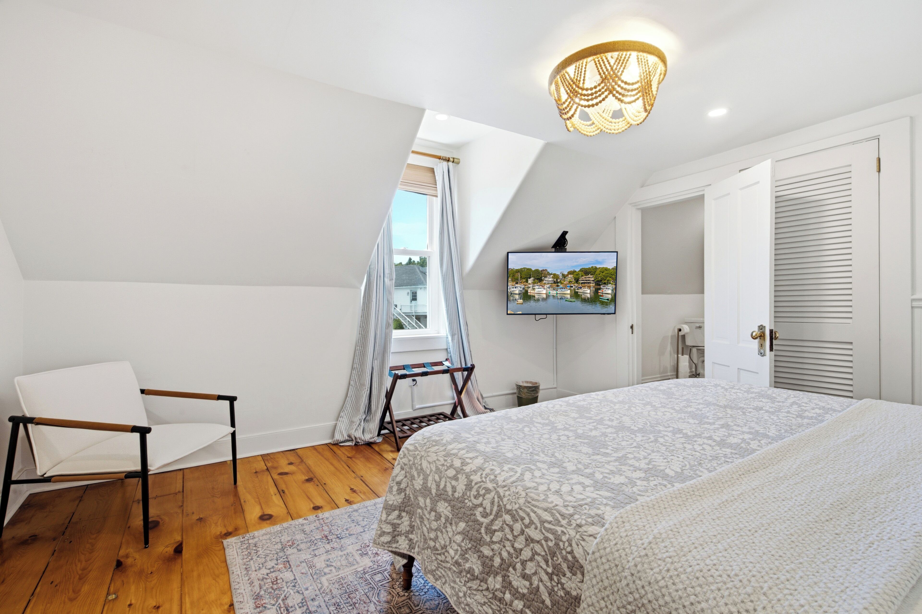 Ein Schlafzimmer mit einem Bett, einem Sessel, einem Fernseher und einem fensterbepflanzten Fenster.