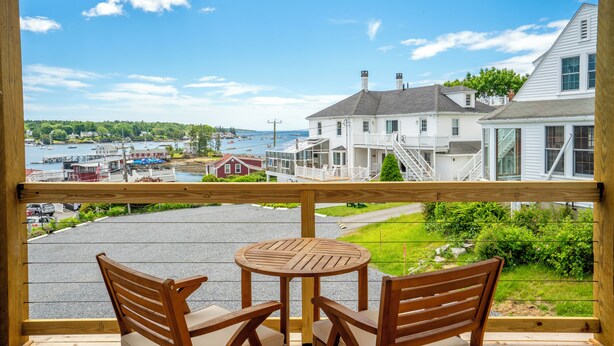 Une terrasse en bois avec une table et des chaises, donnant sur une marina où l’on peut voir des bateaux et des maisons.