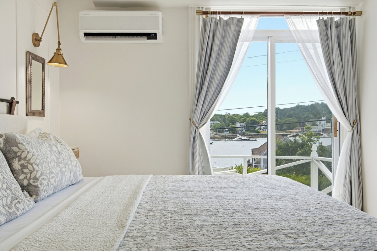 Une chambre à coucher comprenant un lit, une lampe de chevet, un climatiseur, une fenêtre avec des rideaux et une vue sur le paysage urbain.