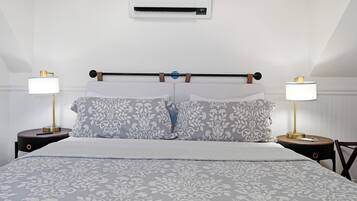 A bedroom with a bed, two bedside tables with lamps, a wall-mounted air conditioner, and a headboard with a towel rack.