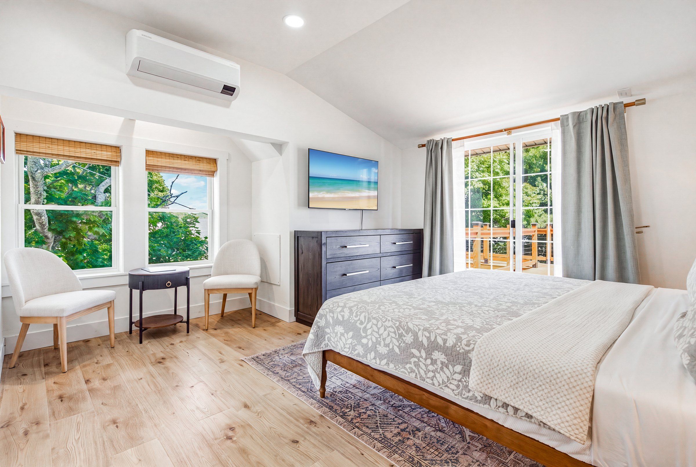 A bedroom with a bed, a desk, two chairs, a dresser, and a TV.