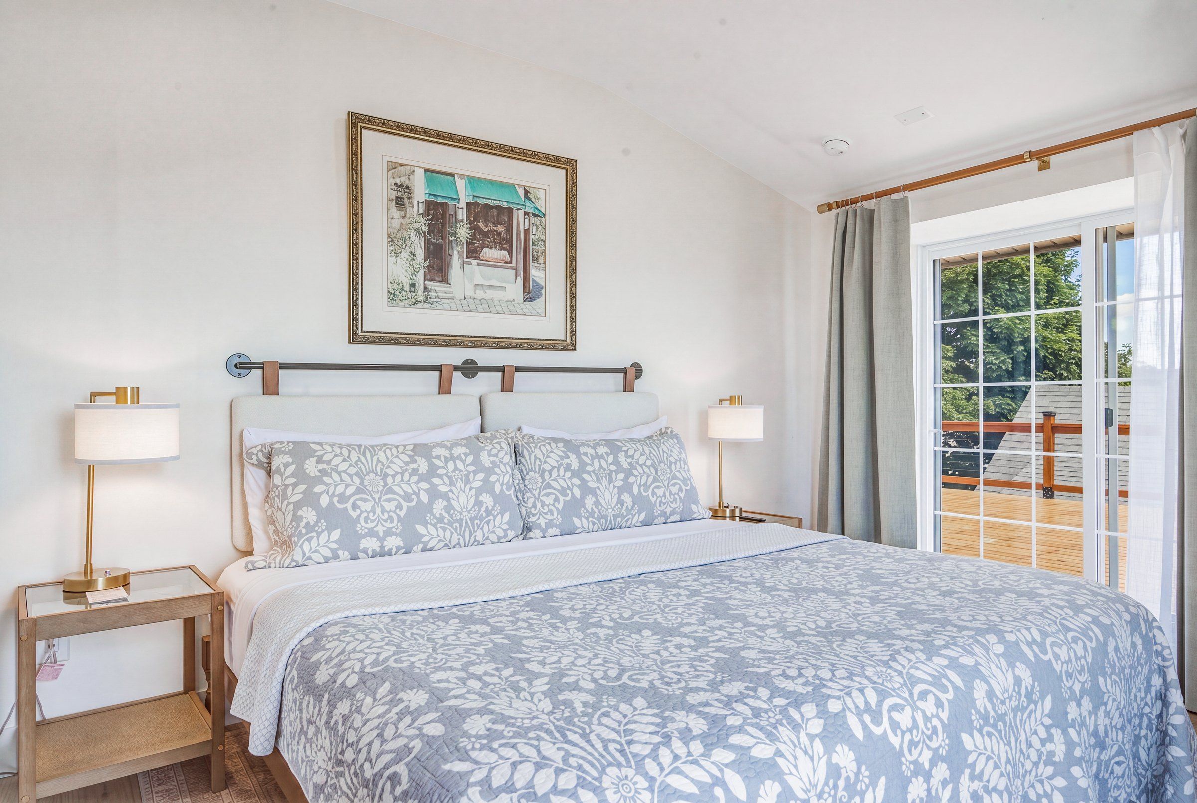 A bedroom with a bed, two bedside tables, a nightstand, a window with curtains, and a framed picture on the wall.