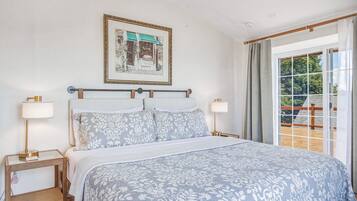 A bedroom with a bed, two bedside tables, a nightstand, a window with curtains, and a framed picture on the wall.