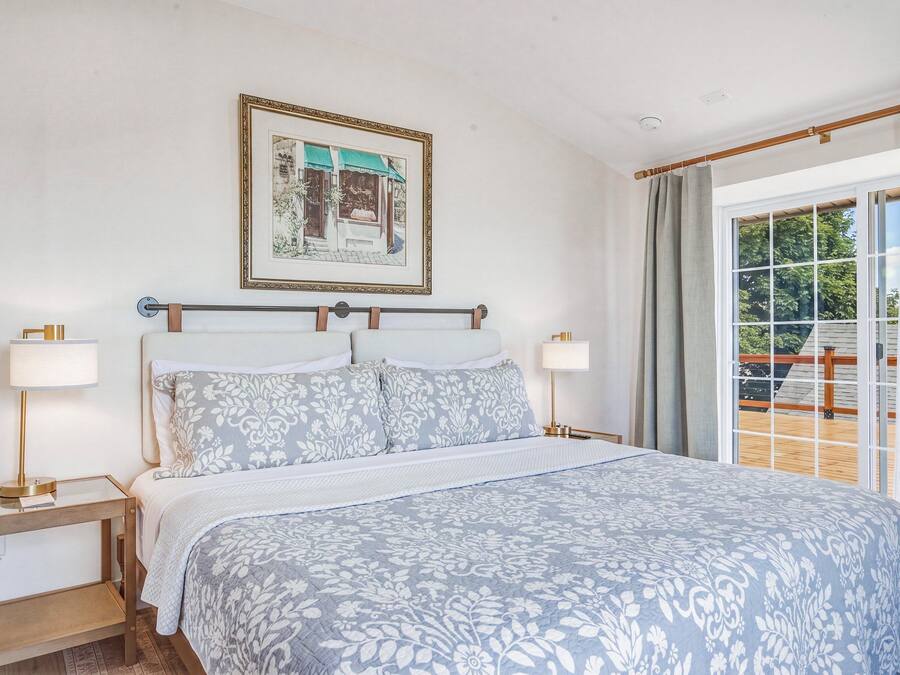 A bedroom with a bed, two bedside tables, a nightstand, a window with curtains, and a framed picture on the wall.