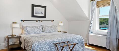 A bedroom with a bed, bedside tables, a picture on the wall, a window with curtains, and a view of greenery outside.