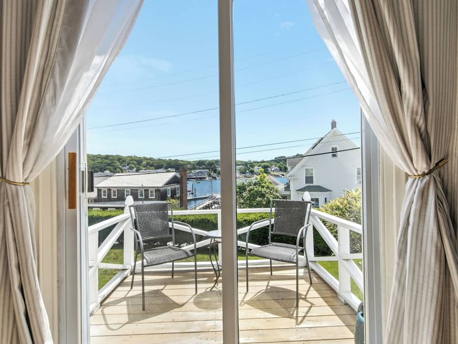 A balcony with two chairs, a white railing, and a view of houses and water.