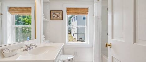 A bathroom with a white sink, toilet, and vanity, a window with a view of a house, and a door with a gold handle.