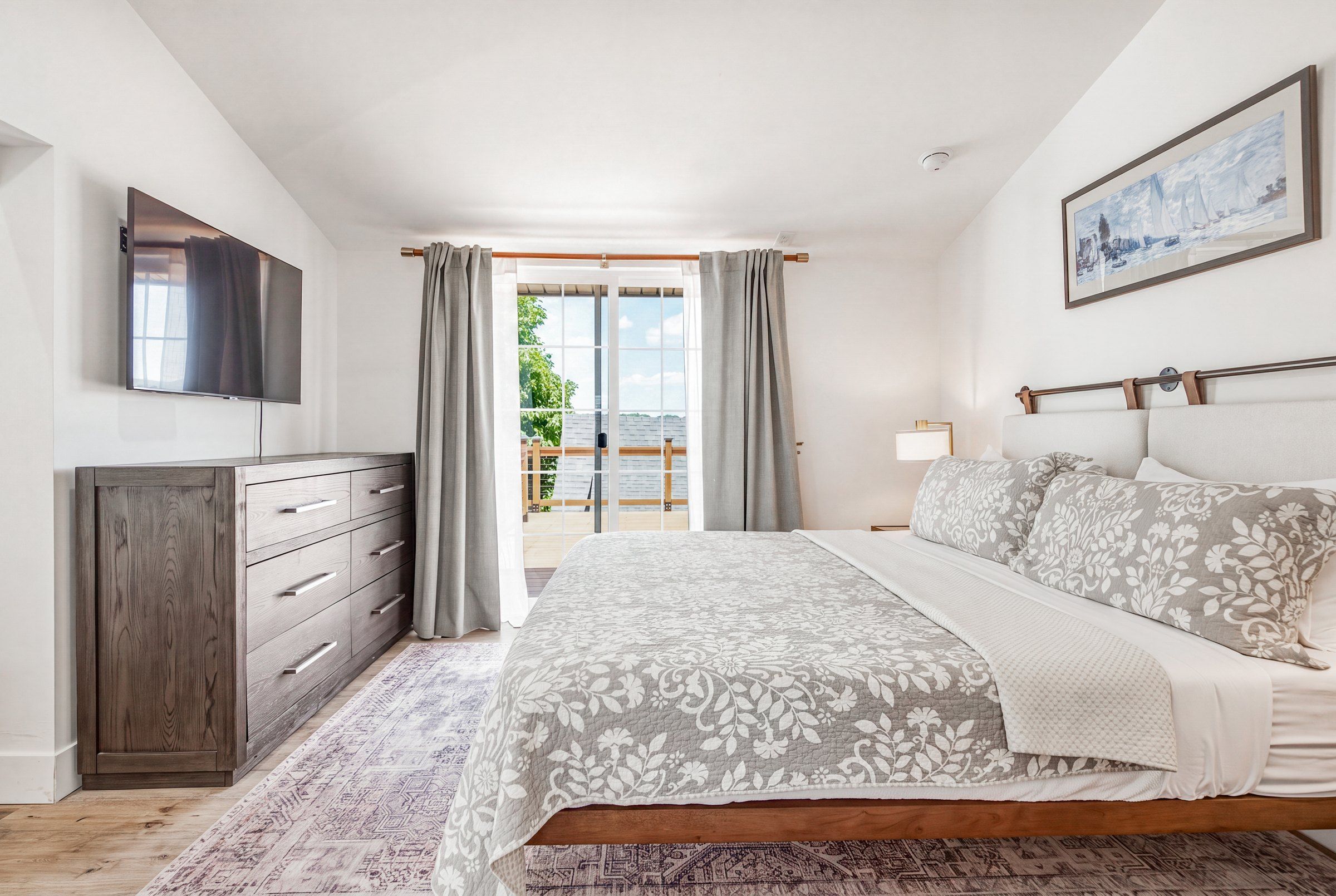 Un dormitorio con una cama, un aparador, un televisor y un cuadro en la pared.