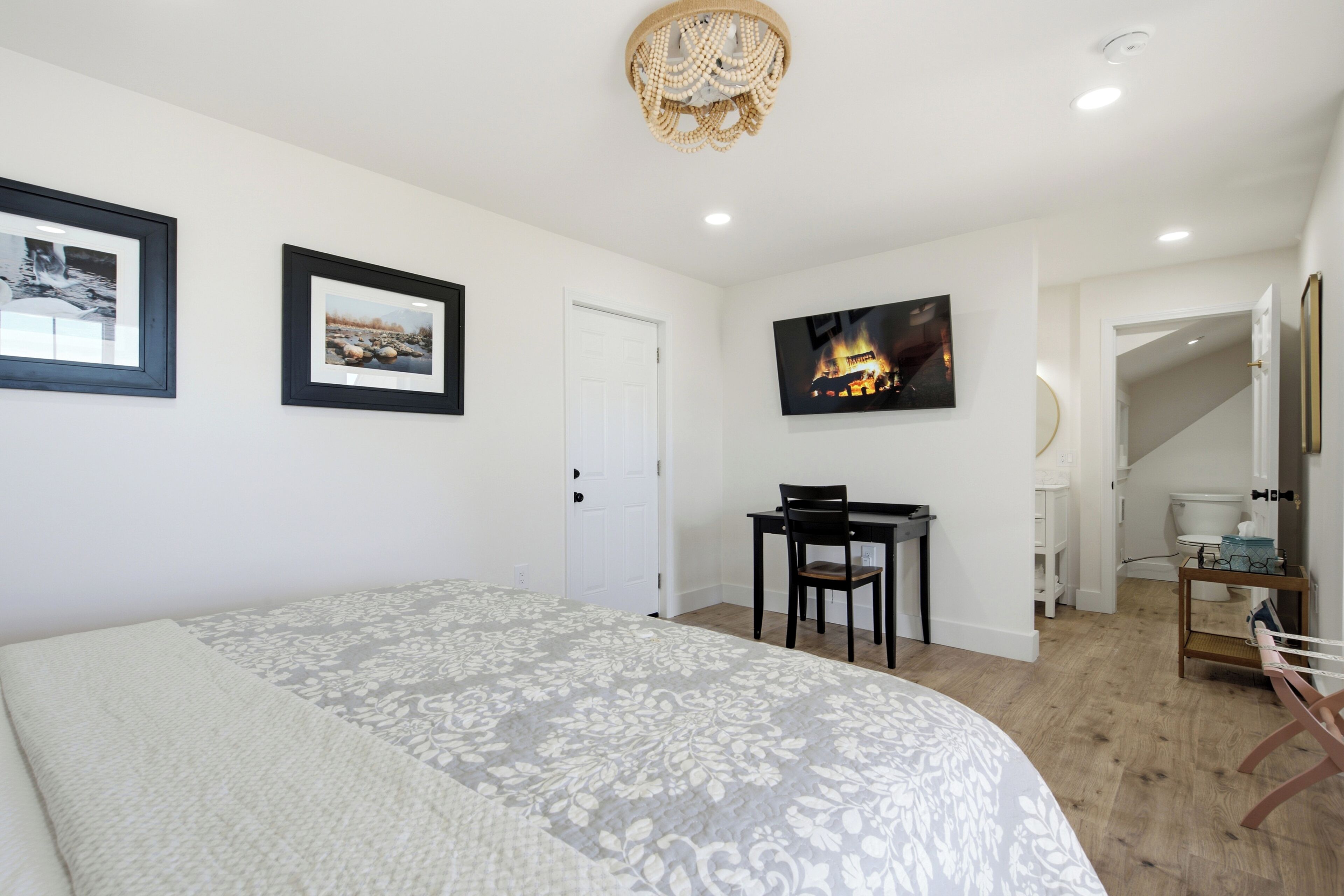 Une chambre à coucher comprenant un lit, un bureau, une chaise, un téléviseur et une porte donnant sur une salle de bain.