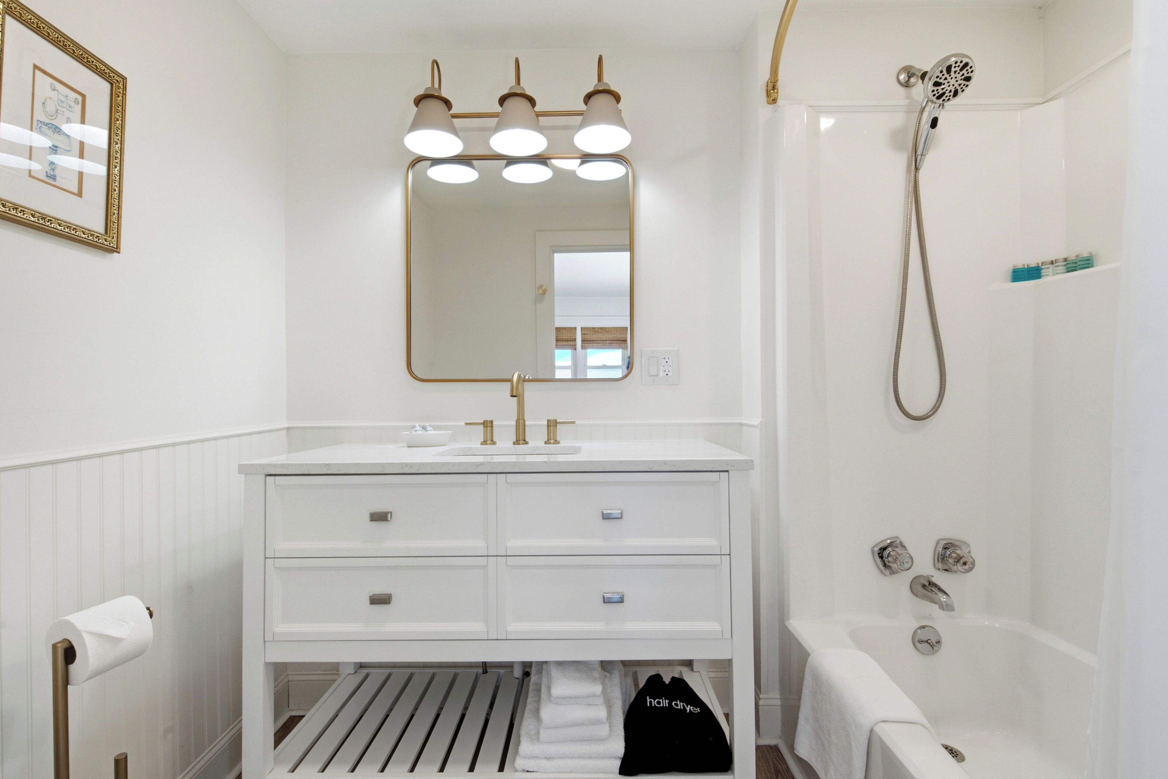 A bathroom with a white vanity, a large mirror, a shower with a handheld showerhead, and a towel rack.