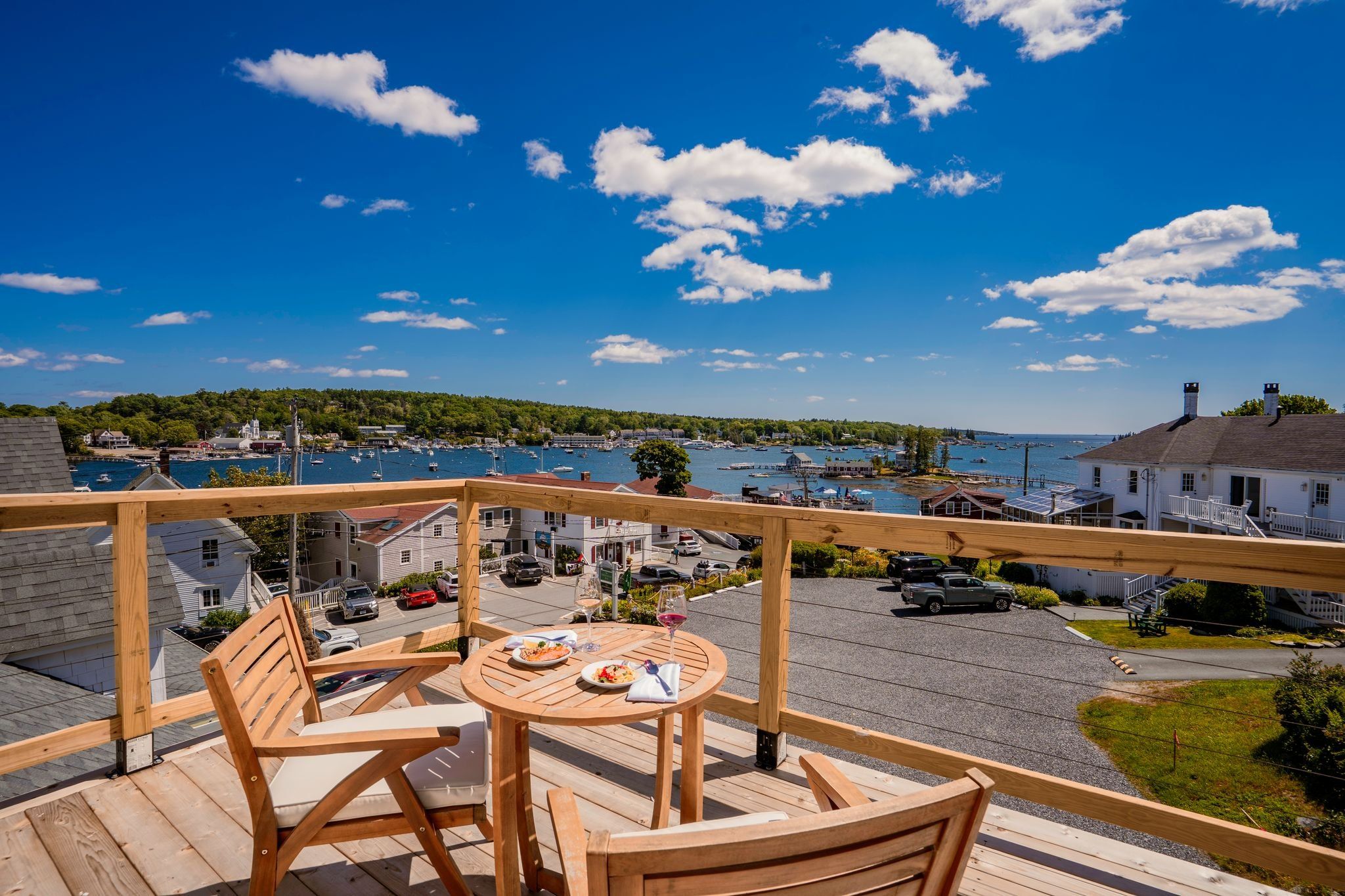 A wooden deck with a table and chairs overlooking a marina with boats and a forested hill in the background.