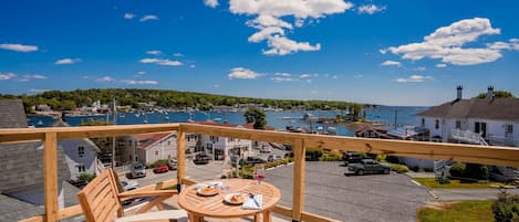 A wooden deck with a table and chairs overlooking a marina with boats and a forested hill in the background.