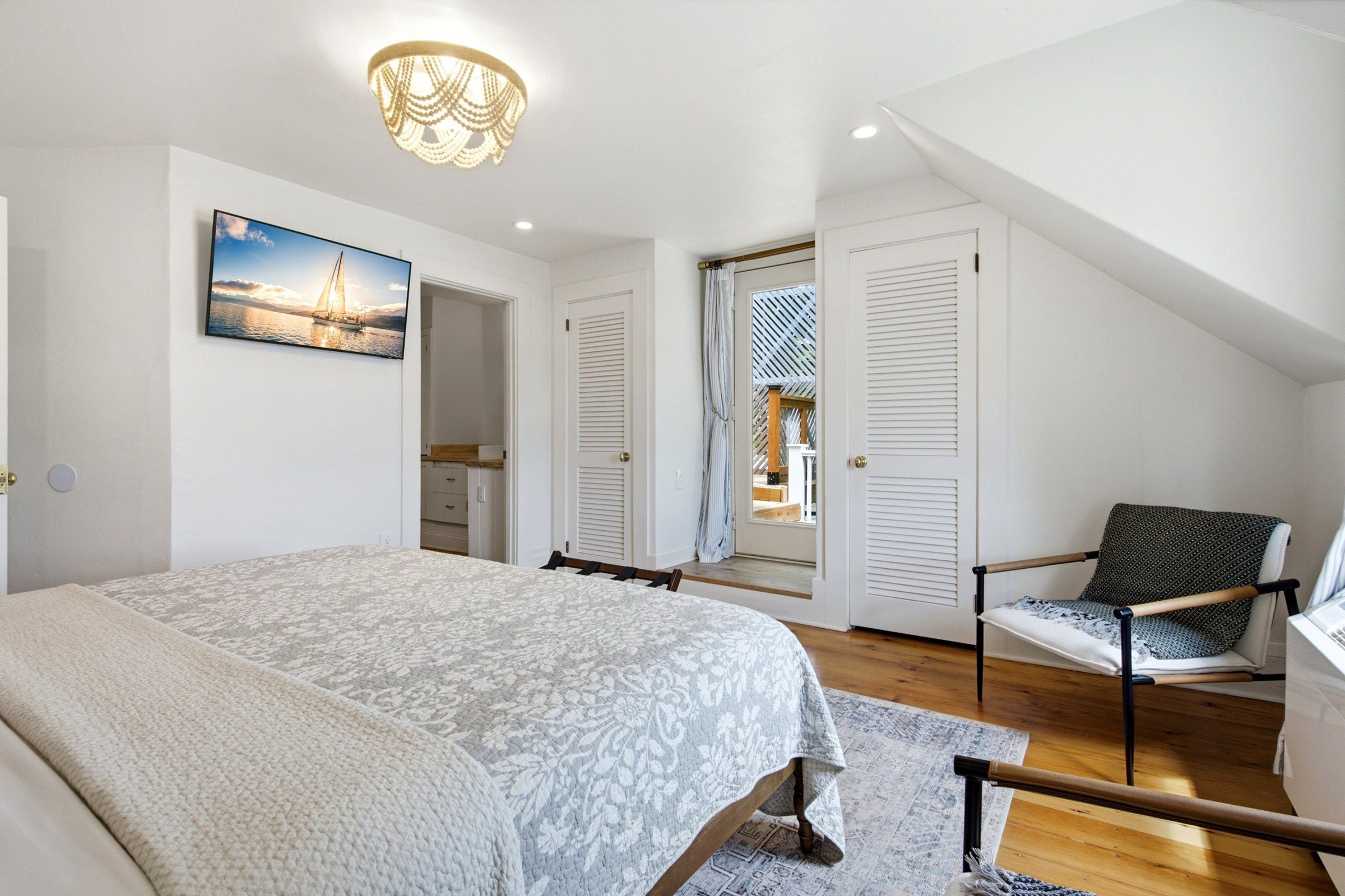 Un dormitorio con cama, una silla, un cuadro y vistas a través de una puerta.