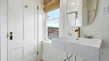 A bathroom with a white sink, a mirror, and a window with a view of buildings.