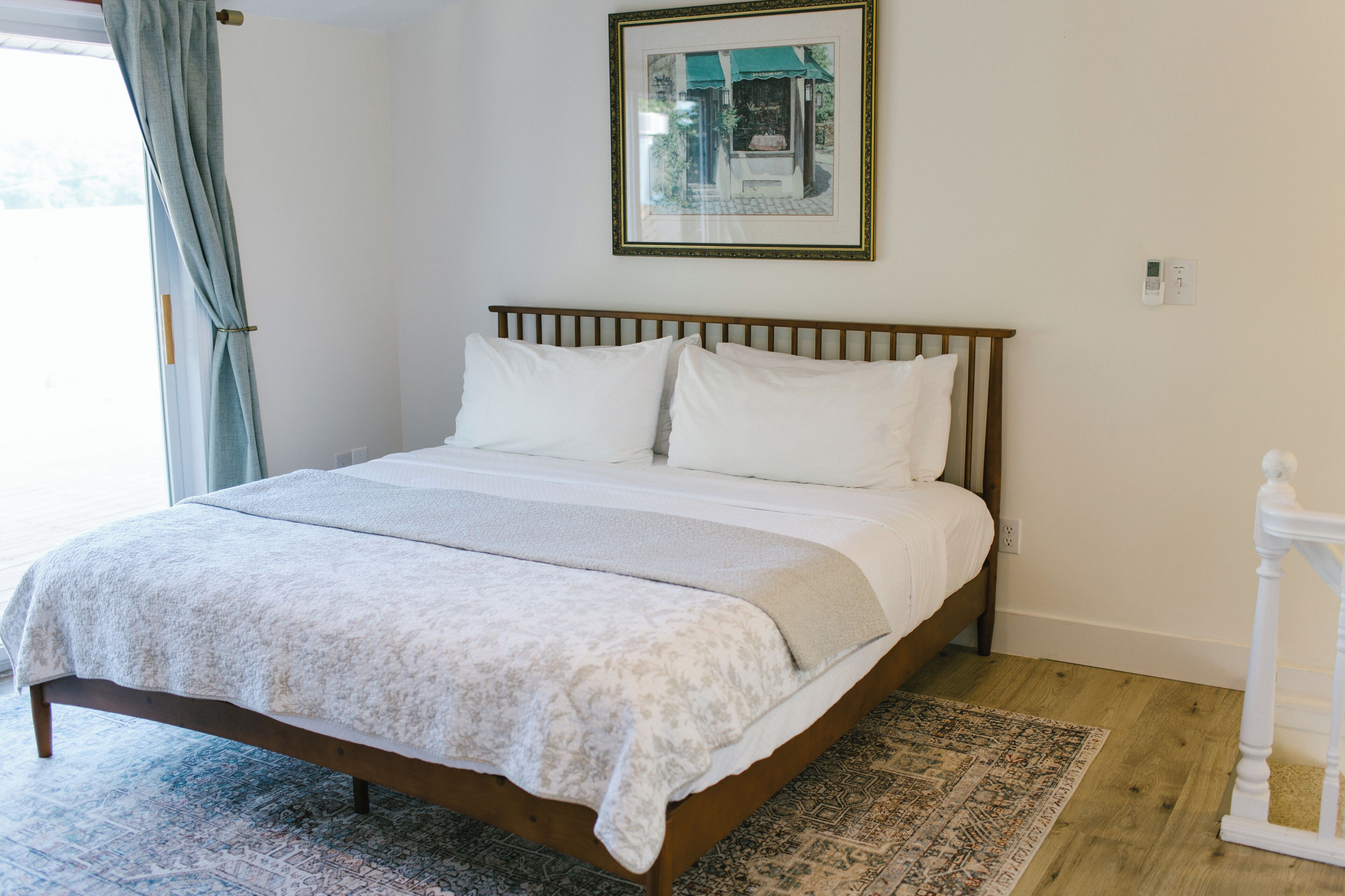 A neatly made bed with a white and gray patterned bedspread, a wooden headboard, and a framed picture above it.