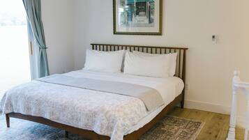 A neatly made bed with a white and gray patterned bedspread, a wooden headboard, and a framed picture above it.