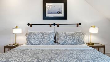 A neatly made bed with a floral-patterned duvet, two bedside lamps, and a framed picture of a sailboat on the wall.