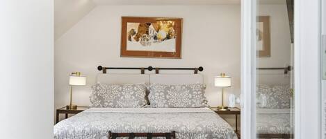 A bedroom with a bed, bedside lamps, a chandelier, a framed picture on the wall, and a mirror.
