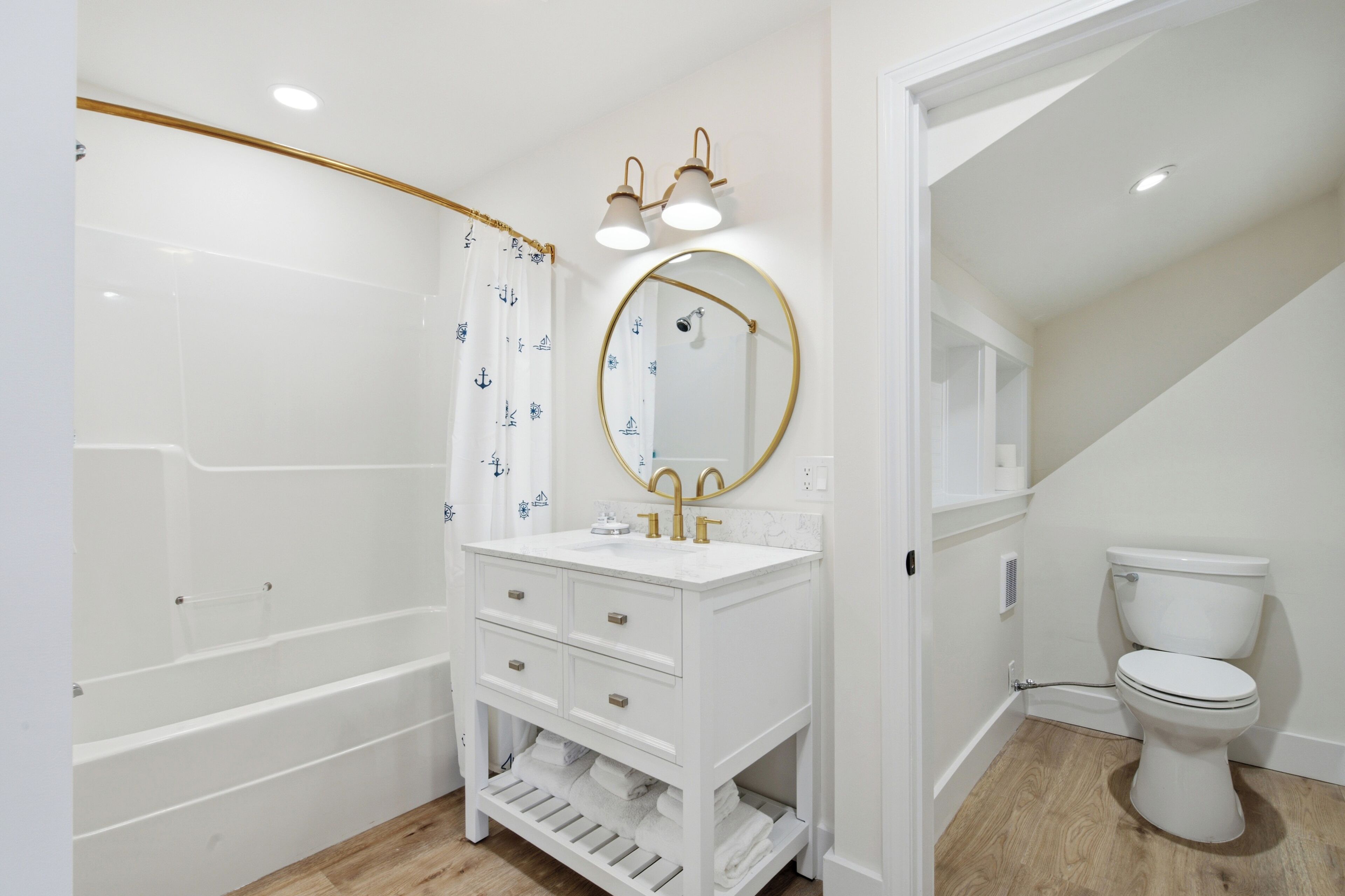A bathroom with a white vanity, a round mirror, a shower curtain with a nautical pattern, and a toilet.