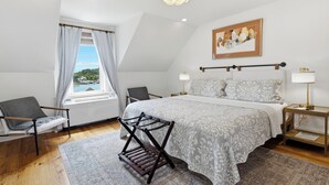 Une chambre à coucher avec un lit, une chaise, une fenêtre avec des rideaux, un lustre, une table de chevet et un tableau au mur.