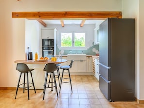 A modern kitchen with a central island, bar stools, a black refrigerator, and a window providing natural light.