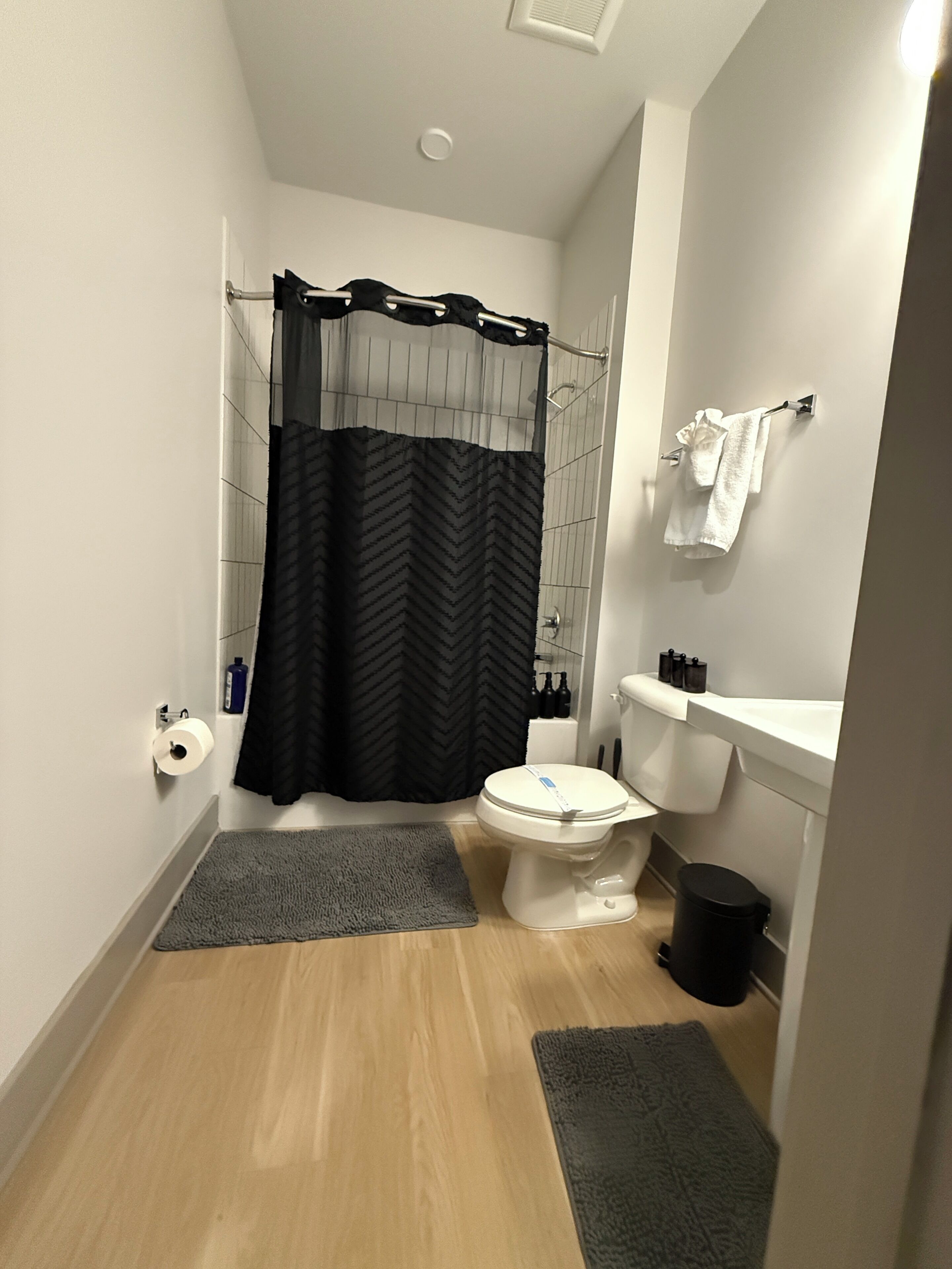 Een badkamer met een toilet, douchegordijn, handdoekrek en een kleine prullenbak.