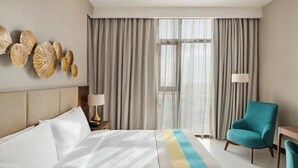 Habitación de hotel con una cama, una silla, una lámpara y vistas al exterior.