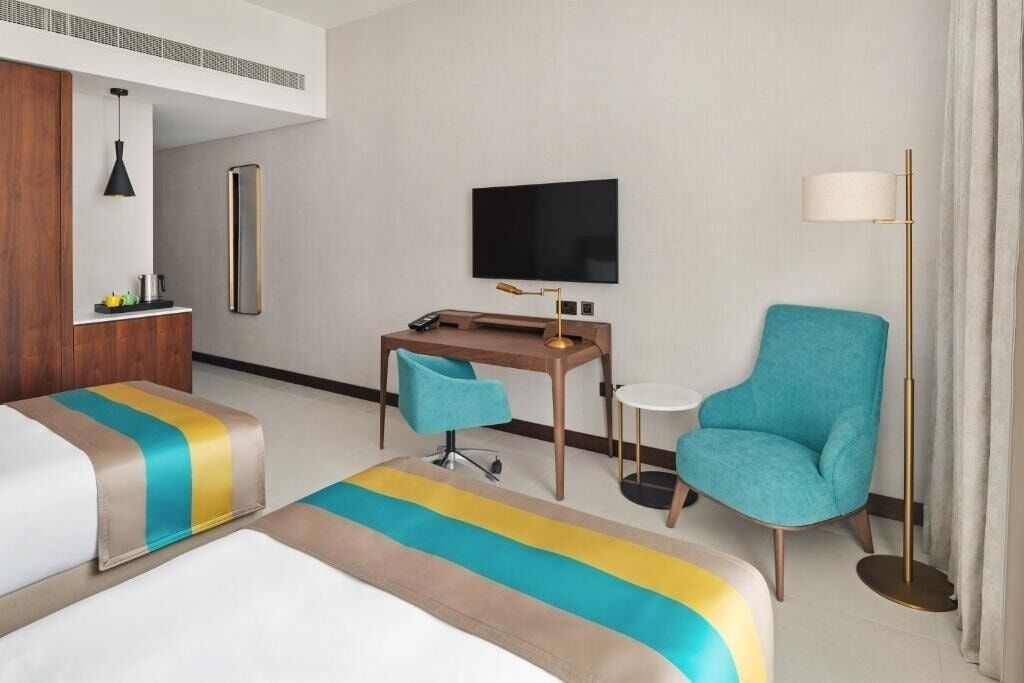 Una camera d'albergo con un letto, una scrivania, una sedia, una televisione e una lampada da terra.