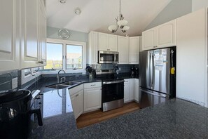 A modern kitchen with white cabinets, stainless steel appliances, a granite countertop, and a view of the outdoors.