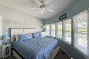 A bedroom with a bed, a nightstand, a lamp, a ceiling fan, and a window with blinds.