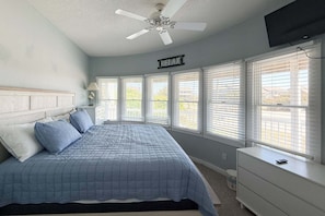 A bedroom with a bed, a ceiling fan, a TV, and a window with blinds.