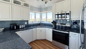 A modern kitchen with white cabinets, a granite countertop, a stainless steel oven, and a microwave. - 2616 - Bay to Breakers - Semi-Oceanfront Retreat w/ Pool & Hot Tub (Duck)