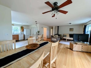 A spacious living area with a dining table, chairs, a sofa, a TV, and a ceiling fan.