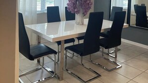 Un coin repas avec une table blanche, des chaises noires et un vase rempli de fleurs violettes.