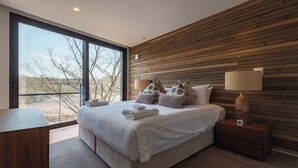 Quarto moderno com uma cama grande, painel de madeira na parede e vista através de uma janela ampla.