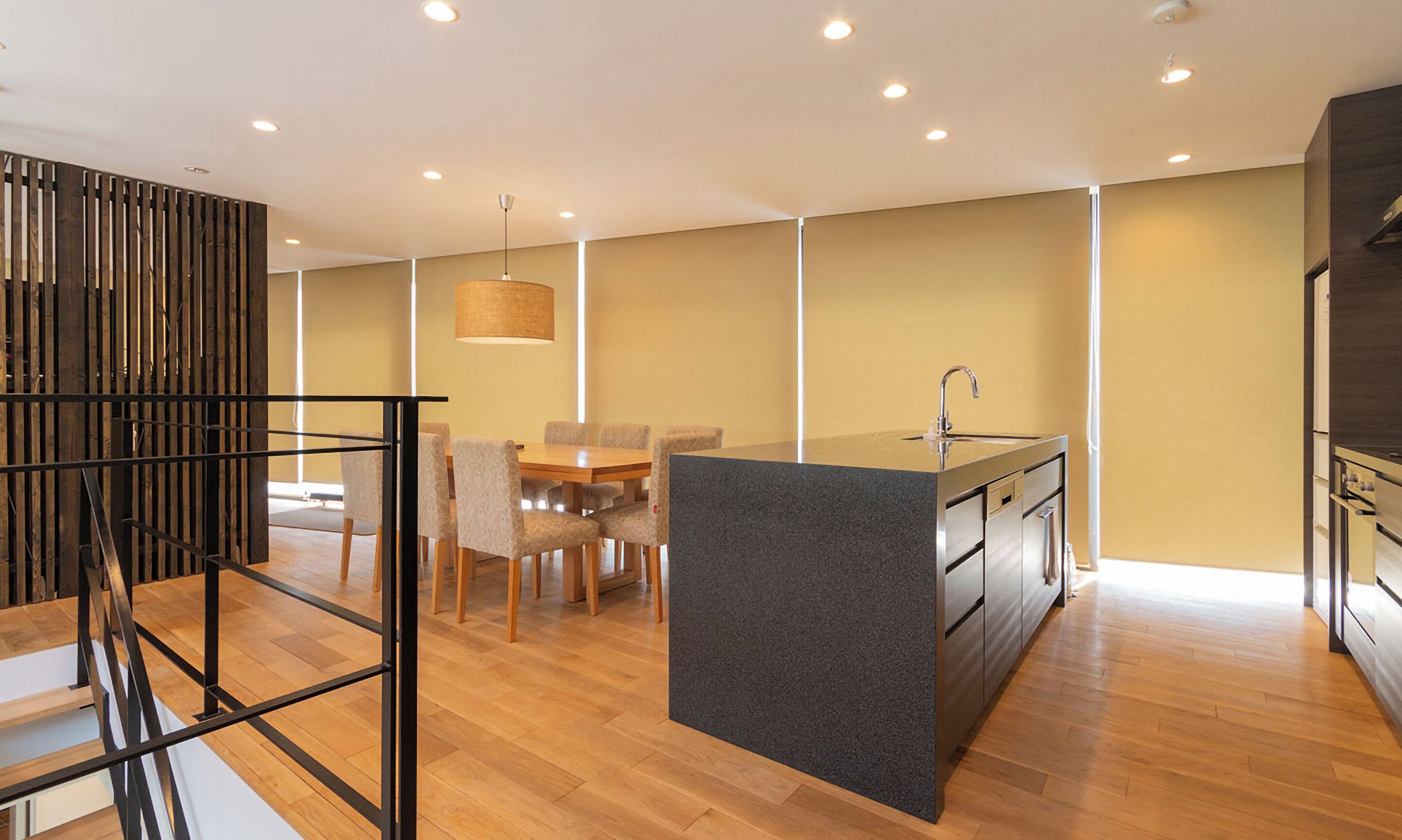A modern kitchen with a central island, wooden flooring, and a dining area with chairs and a table.