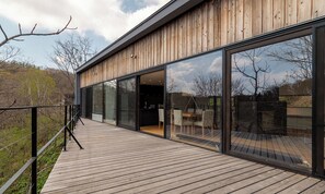 Un bâtiment moderne doté de grandes fenêtres en verre, d’une terrasse en bois et offrant une vue sur le paysage environnant.