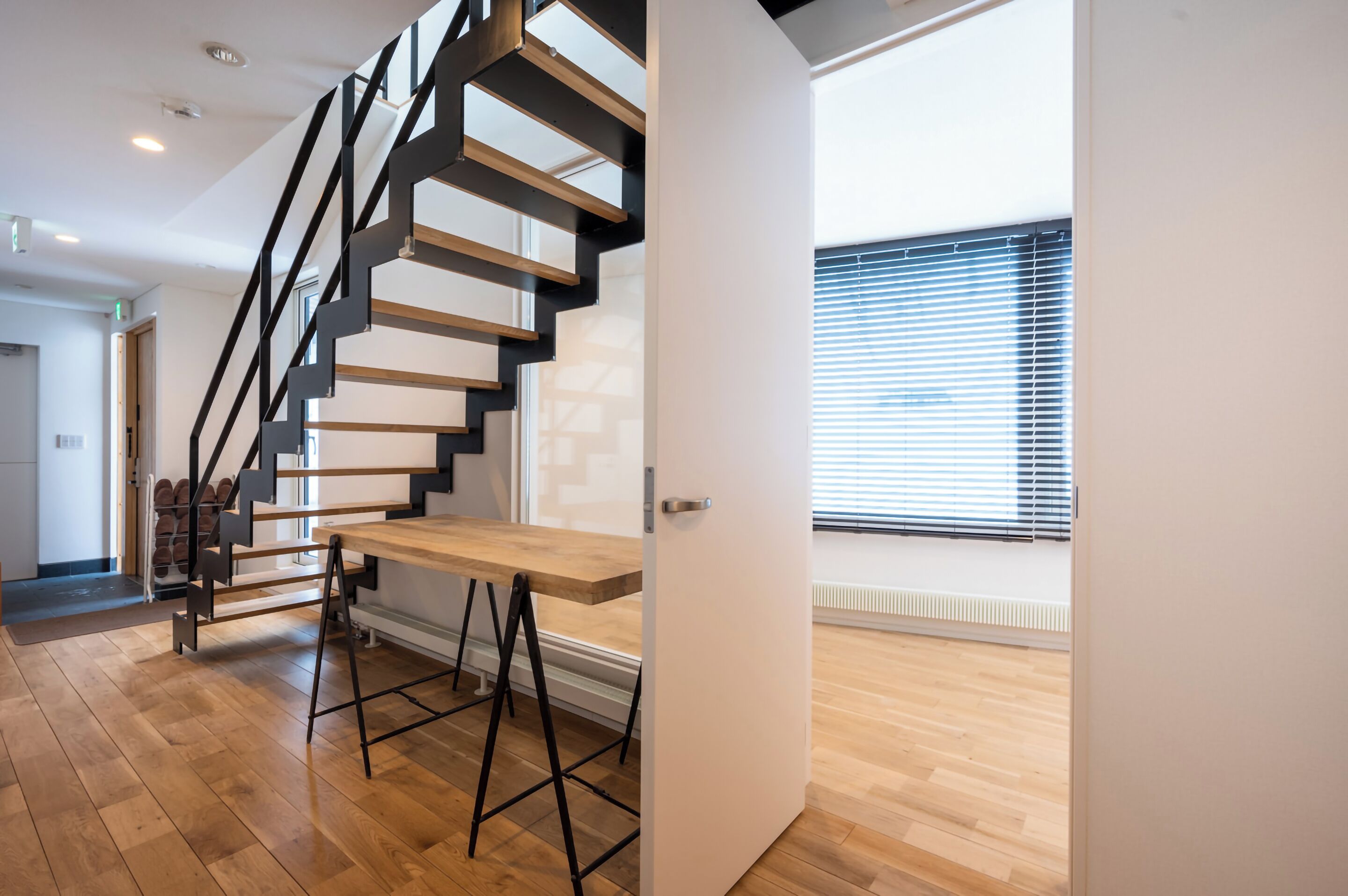 A modern interior with a wooden staircase, a white door, and a window with blinds.