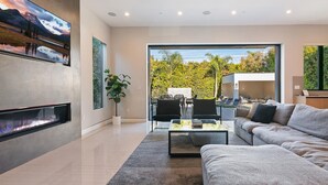 A modern living room with a fireplace, a sofa, a coffee table, and a view of a garden and outdoor seating area. - Chic 4-bedroom villa with WiFi, AC in vibrant Los Angeles (Los Angeles)