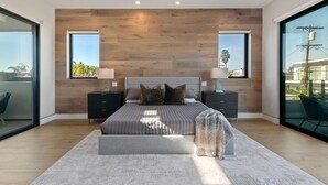 A modern bedroom with a large bed, two nightstands, a grey rug, and a view of the outdoors through large windows. - Chic 4-bedroom villa with WiFi, AC in vibrant Los Angeles (Los Angeles)