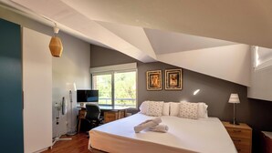 Ein Schlafzimmer mit Bett, Schreibtisch, Stuhl, Computer und Fenster.