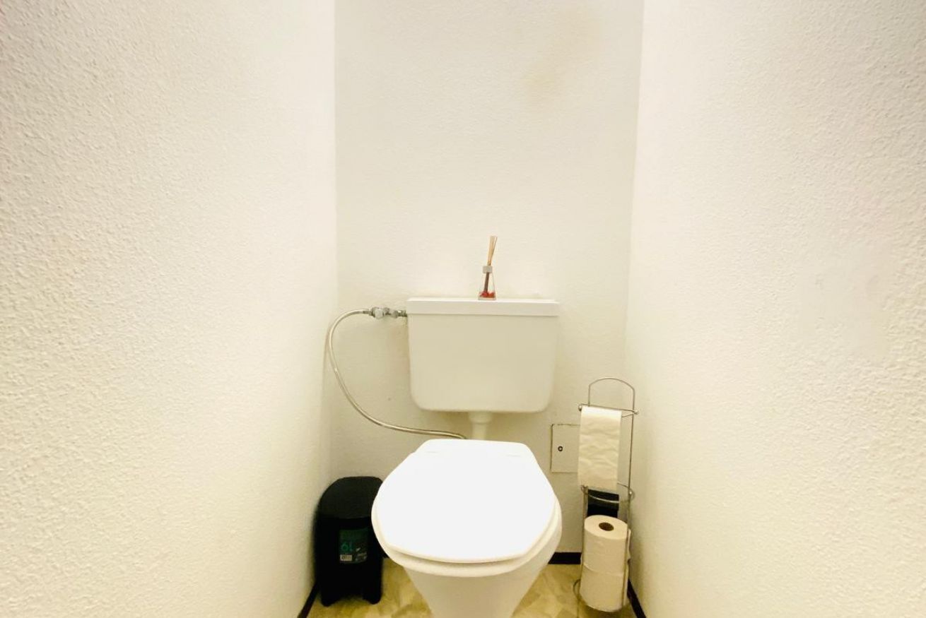 A small bathroom with a white toilet, a black trash bin, and a toilet paper holder.