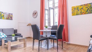 Uma sala de estar moderna com sofá, mesa de centro e cadeiras, mesa de jantar, janela com cortinas e duas obras de arte nas paredes.