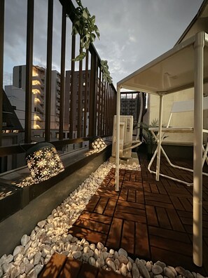 A rooftop terrace with a seating area, a decorative light fixture, and a view of surrounding buildings.